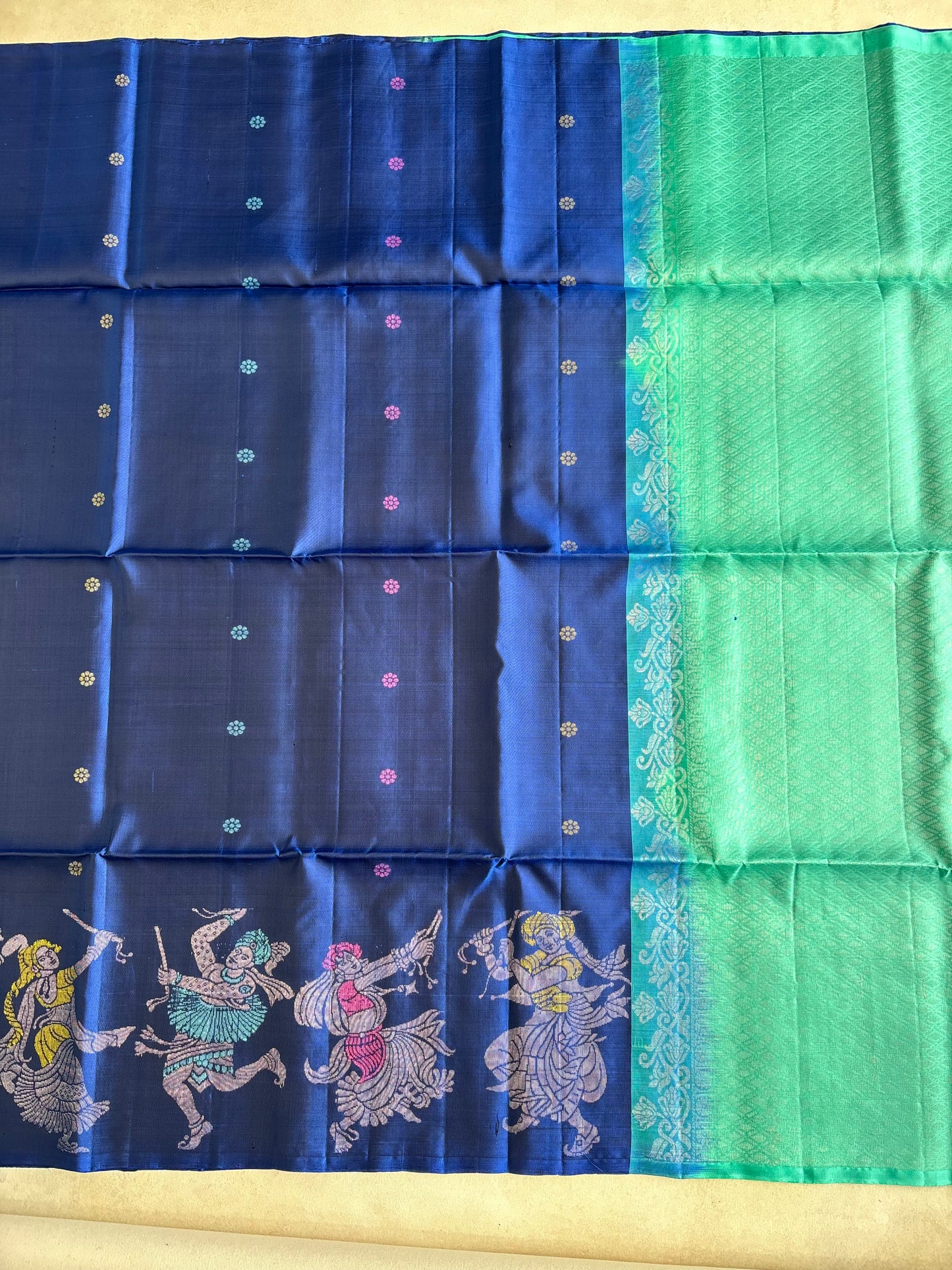A blue and green silk saree with intricate zari embroidery and traditional Indian motifs, laid flat on a beige surface.