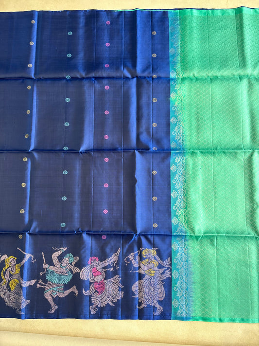 A blue and green silk saree with intricate zari embroidery and traditional Indian motifs, laid flat on a beige surface.