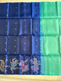 A blue and green silk saree with intricate zari embroidery and traditional Indian motifs, laid flat on a beige surface.